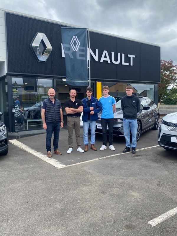 Cinq personnes se tiennent devant une concession Renault. Des voitures sont visibles.
