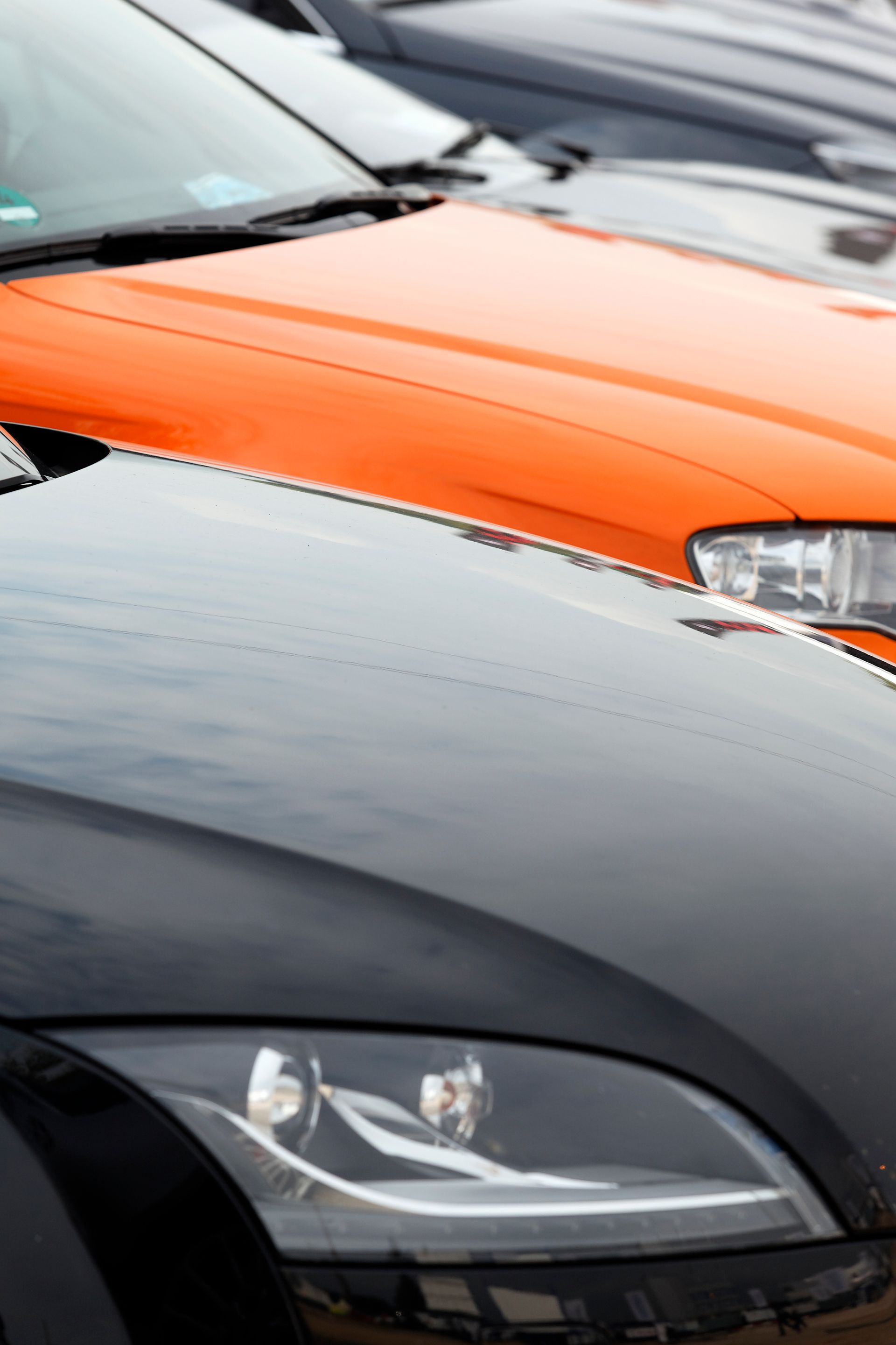 Rangée de voitures garées ; une voiture noire au premier plan, une voiture orange au milieu et une voiture grise à l'arrière-plan.