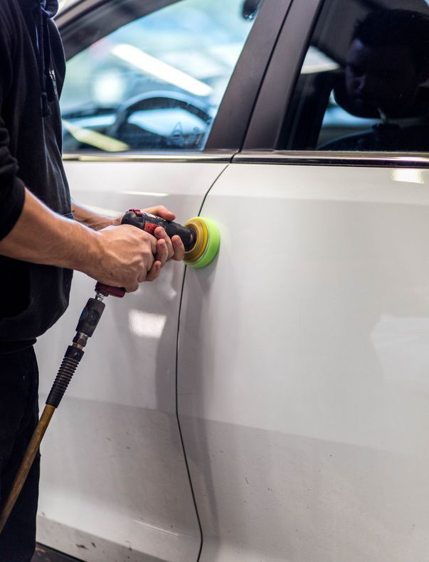 Une personne utilise une polisseuse pour polir une portière de voiture blanche dans un garage.