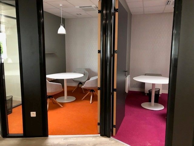 Salon de bureau moderne avec portes vitrées, moquette orange et magenta et petites tables rondes avec chaises