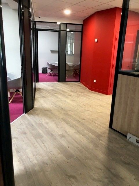 Couloir de bureau moderne avec des pièces aux parois vitrées, un parquet et un mur rouge vif.