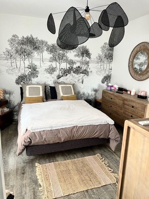 Chambre confortable avec un lit, un tapis tissé, une commode et des suspensions noires sur un mur orné d'une fresque d'arbre.