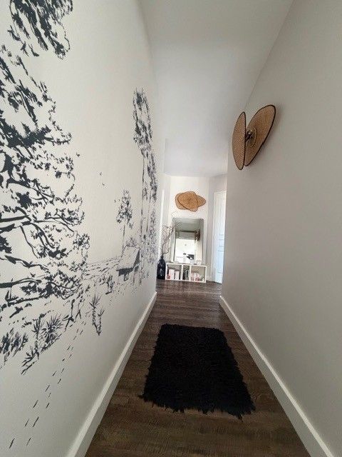 Couloir étroit avec tapis noir, art mural abstrait et miroir au fond.
