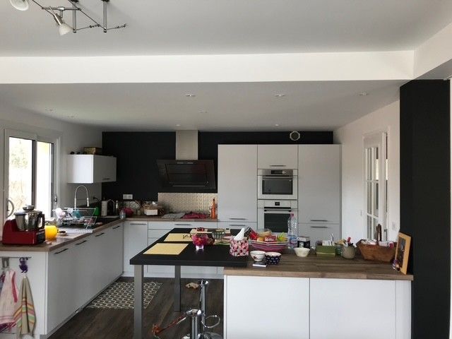 Cuisine moderne avec placards noirs et blancs, îlot central et grandes fenêtres laissant entrer la lumière naturelle