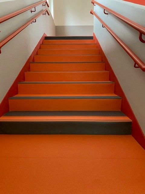 Escalier orange avec rampes rouges et marches grises montant