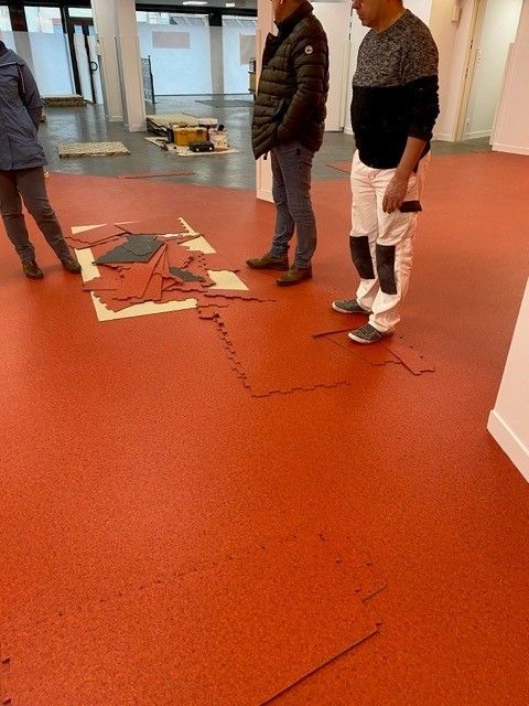Des personnes se tiennent debout dans le hall d'un immeuble, à côté de carreaux cassés éparpillés sur un sol orange.