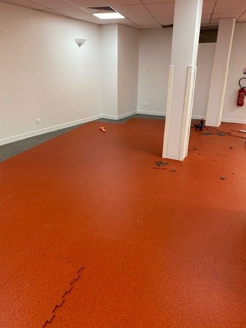 Pièce vide au sous-sol avec sol orange, piliers blancs et extincteur fixé au mur