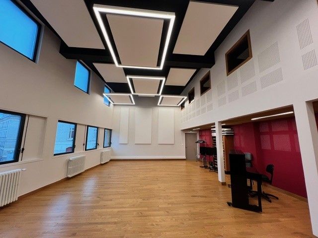 Bureau moderne à aire ouverte avec parquet, éclairage au plafond, fenêtres bleues et alcôve de réunion rose.