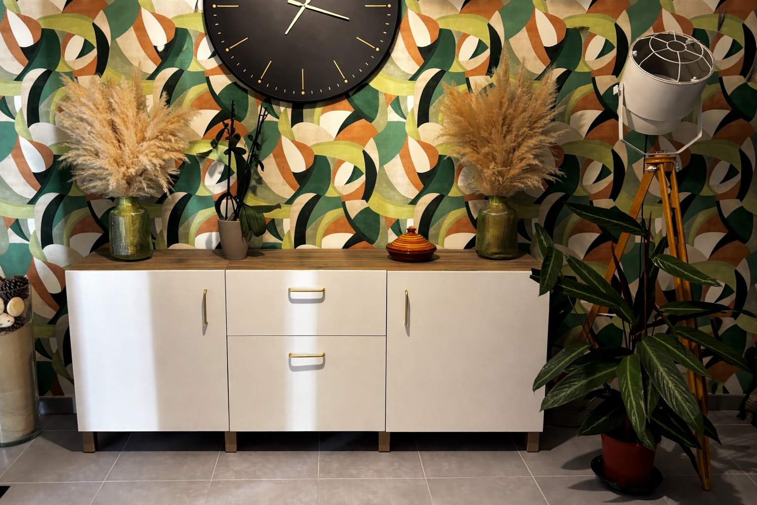 Buffet blanc avec compositions florales séchées, grande horloge murale et papier peint à motifs dans une pièce moderne