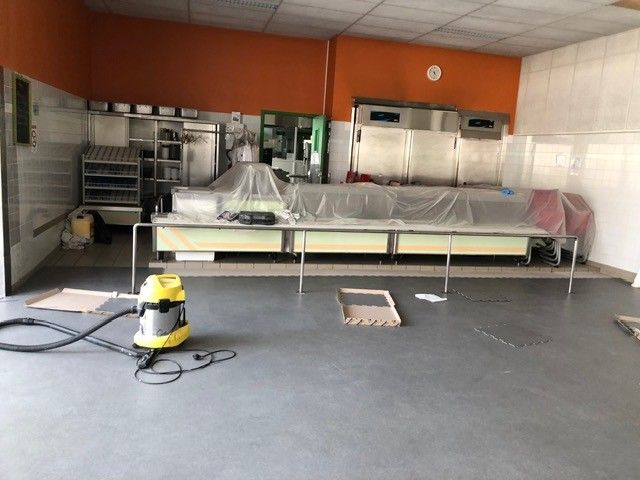 Cuisine industrielle avec comptoirs en acier inoxydable, murs orange et autolaveuse au premier plan