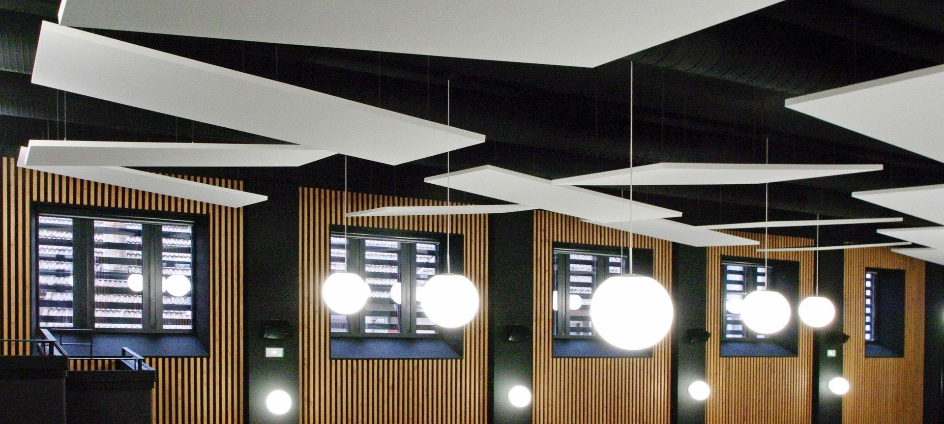 Intérieur moderne avec murs lambrissés, panneaux de plafond géométriques et suspensions lumineuses rondes