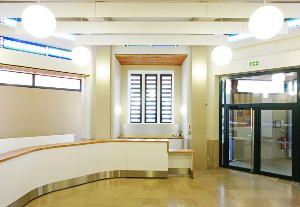 Hall d'entrée moderne et lumineux avec bureau blanc incurvé, luminaires suspendus en forme de globe, parquet et portes d'entrée vitrées