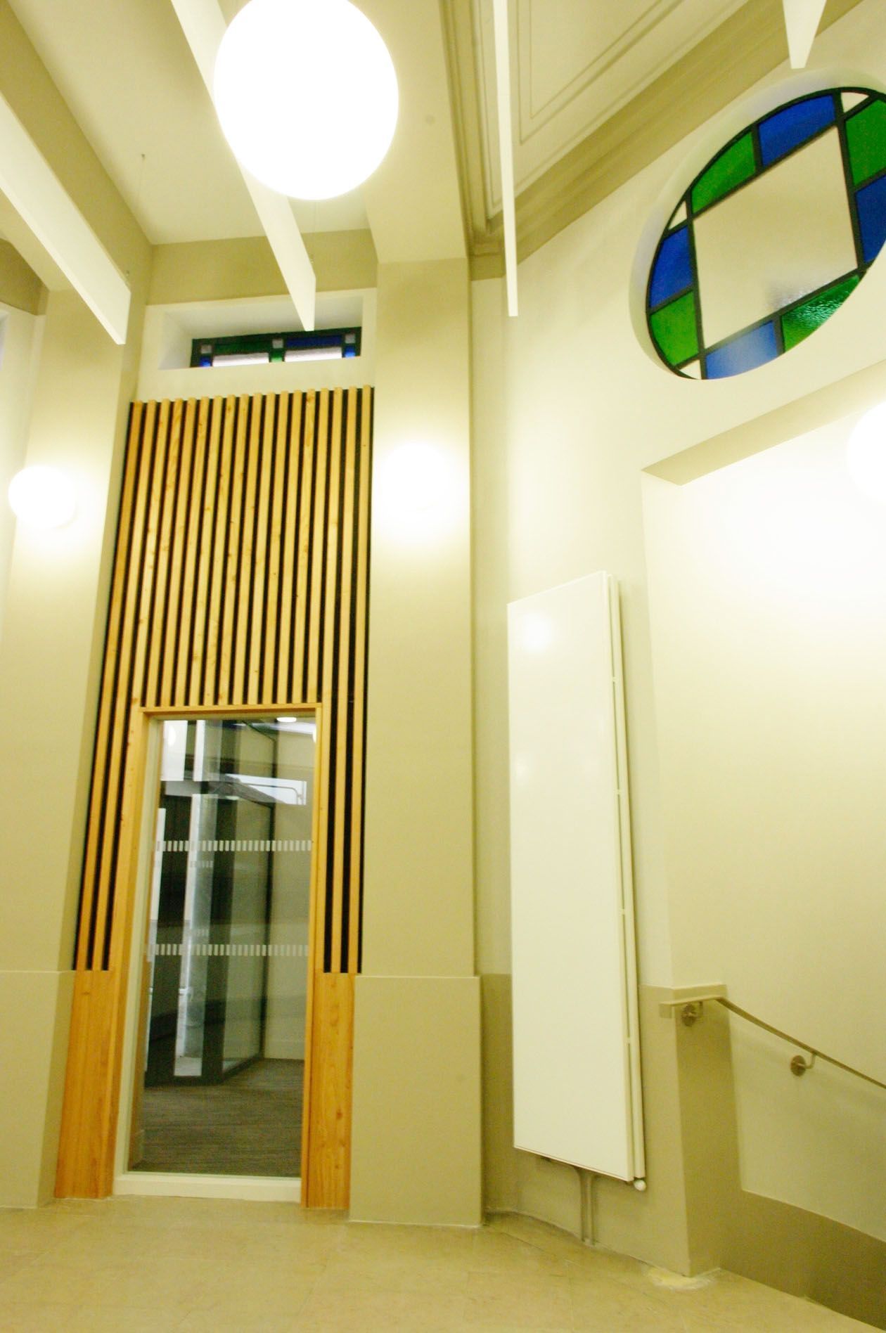 Cage d'escalier intérieure avec murs beiges, lattes de bois, porte d'ascenseur et œuvre d'art murale ronde près du plafond