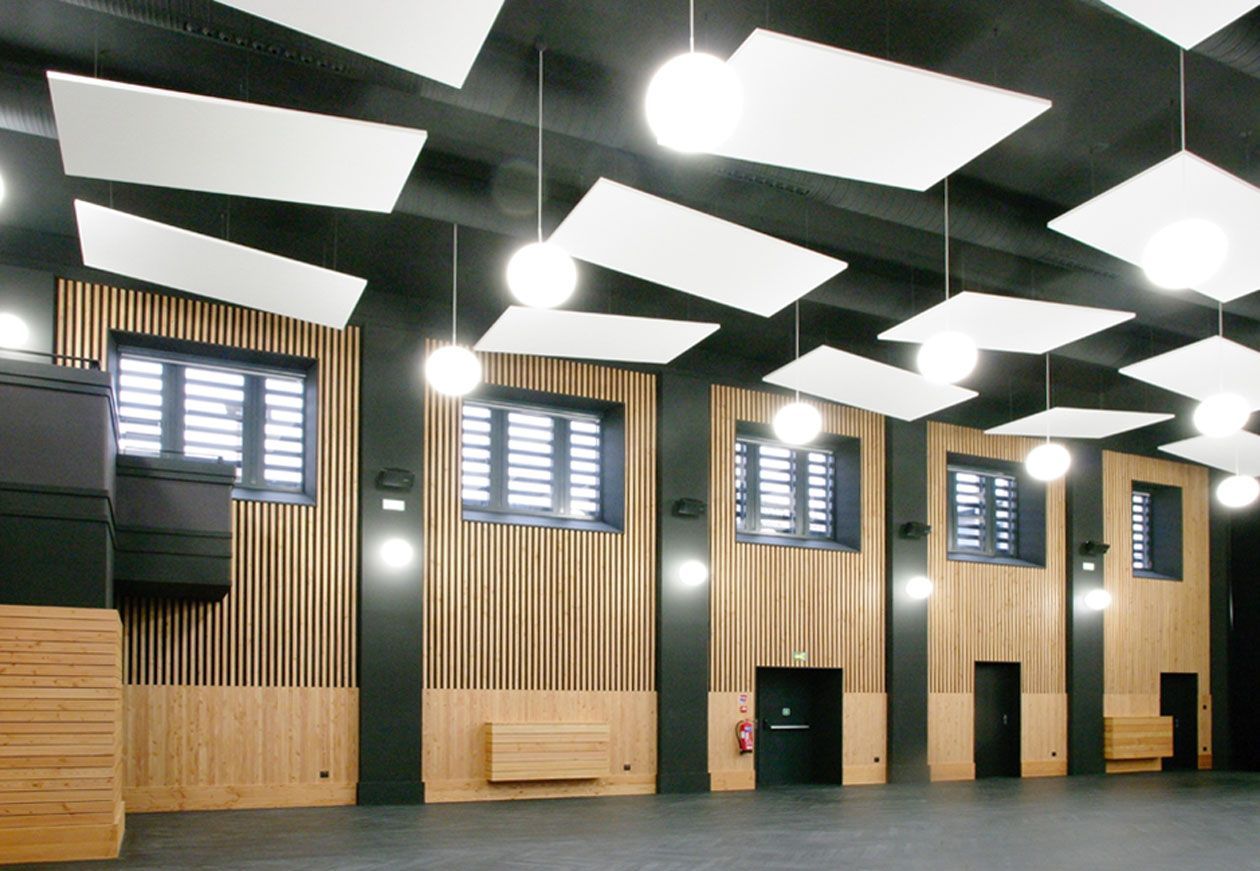 Hall intérieur vide avec murs lambrissés, poutres noires au plafond et puits de lumière.