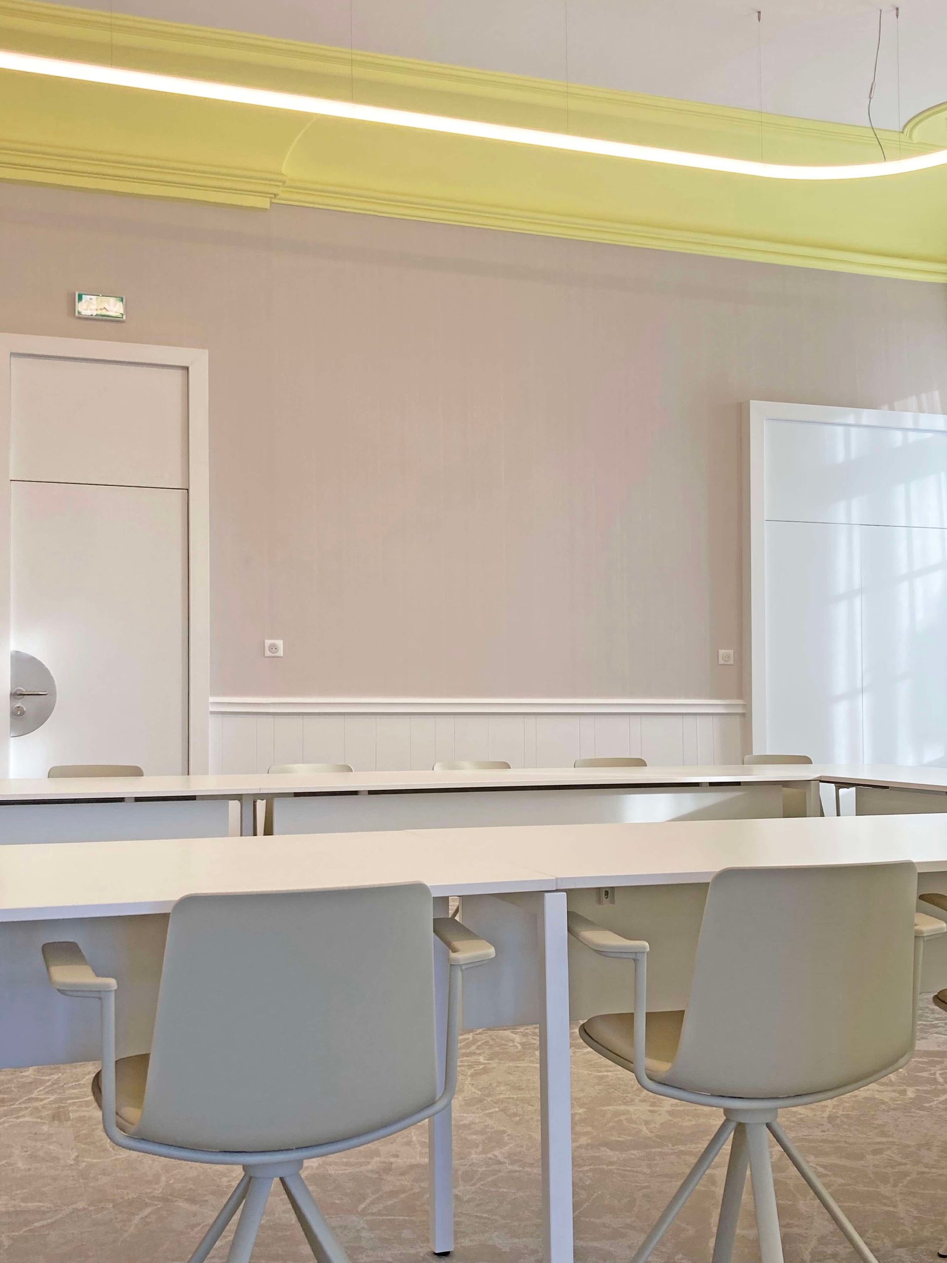 Salle du conseil à Bessines vide avec chaises grises, tables blanches et murs clairs sous un plafond éclairé en jaune