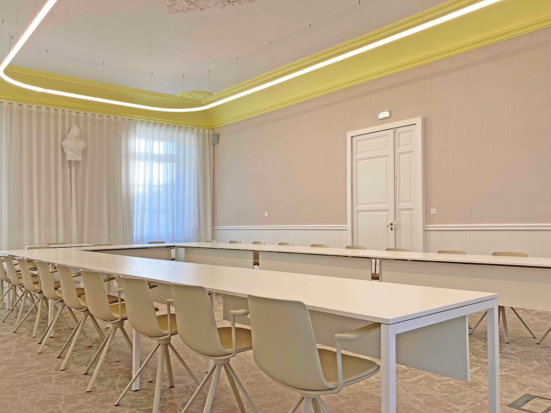 Salle du conseil à Bessines vide avec de longues tables, des chaises blanches et des murs beige clair.