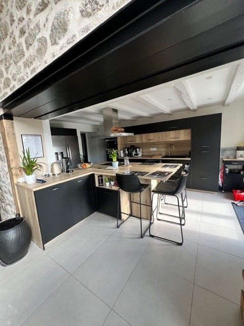 Cuisine moderne ouverte avec placards noirs, éléments en bois, tabourets de bar et grand carrelage gris au sol