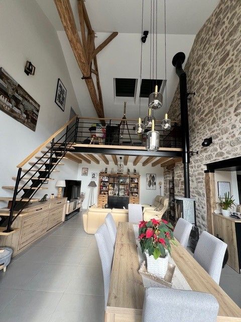 Salle à manger lumineuse de type loft avec haut plafond, escalier en mezzanine, mur en pierre et chaises blanches