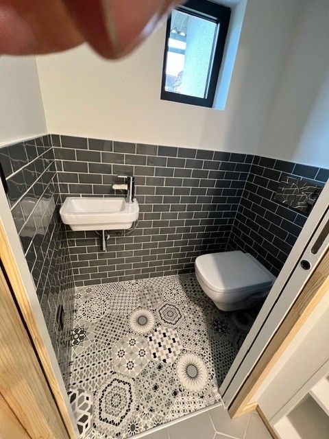Petite salle de bains carrelée avec lavabo mural, toilettes et carrelage au sol à motifs.