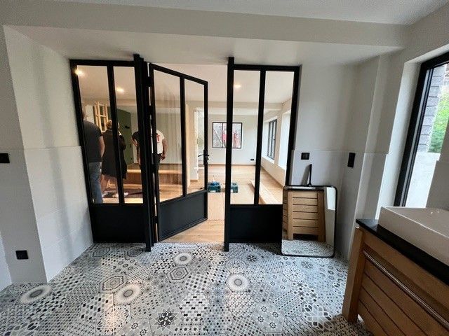Pièce moderne avec sol carrelé à motifs, portes vitrées à cadre noir et armoire en bois près d'une fenêtre