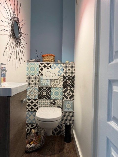 Petite salle de bains avec des toilettes adossées à un mur carrelé de carreaux à motifs colorés et des murs bleus.