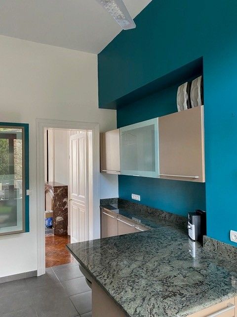 Cuisine moderne avec murs bleu sarcelle, comptoirs en granit, armoires blanches et une porte donnant sur une autre pièce