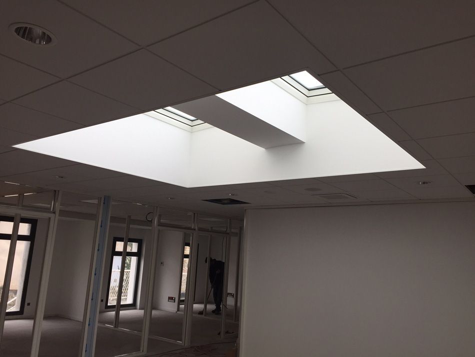 Plafond de bureau avec une grande verrière carrée et des éclairages fluorescents au-dessus de pièces aux parois vitrées