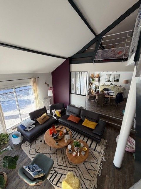 Salon lumineux avec canapés noirs, table basse ronde, tapis rayé et vue sur l'océan à travers de grandes fenêtres
