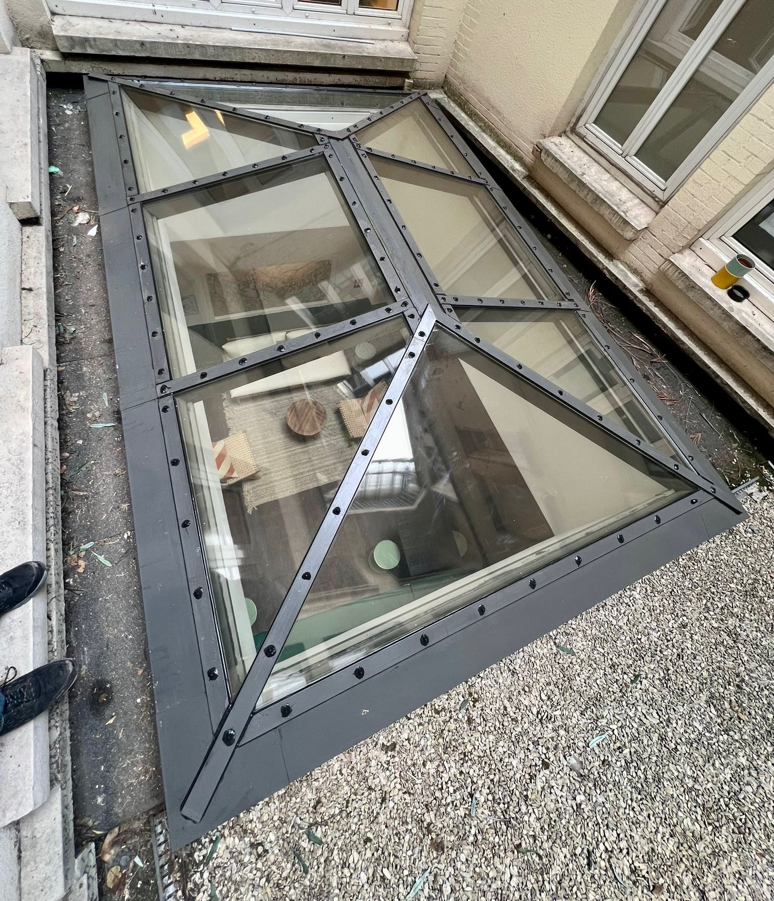 Puits de lumière incliné en verre, avec un cadre en métal foncé.