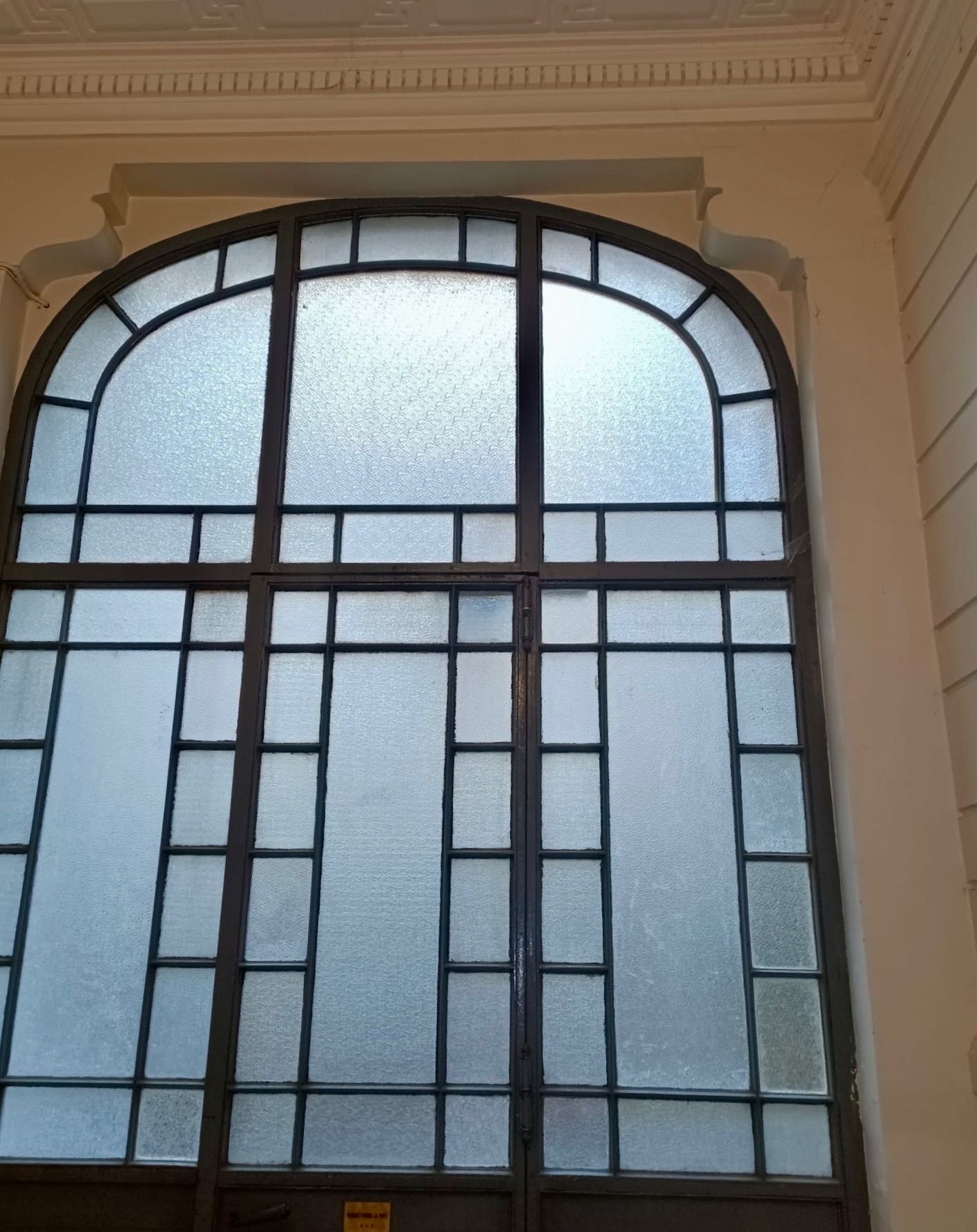 Grande fenêtre cintrée en verre dépoli à grille noire, dans un bâtiment.