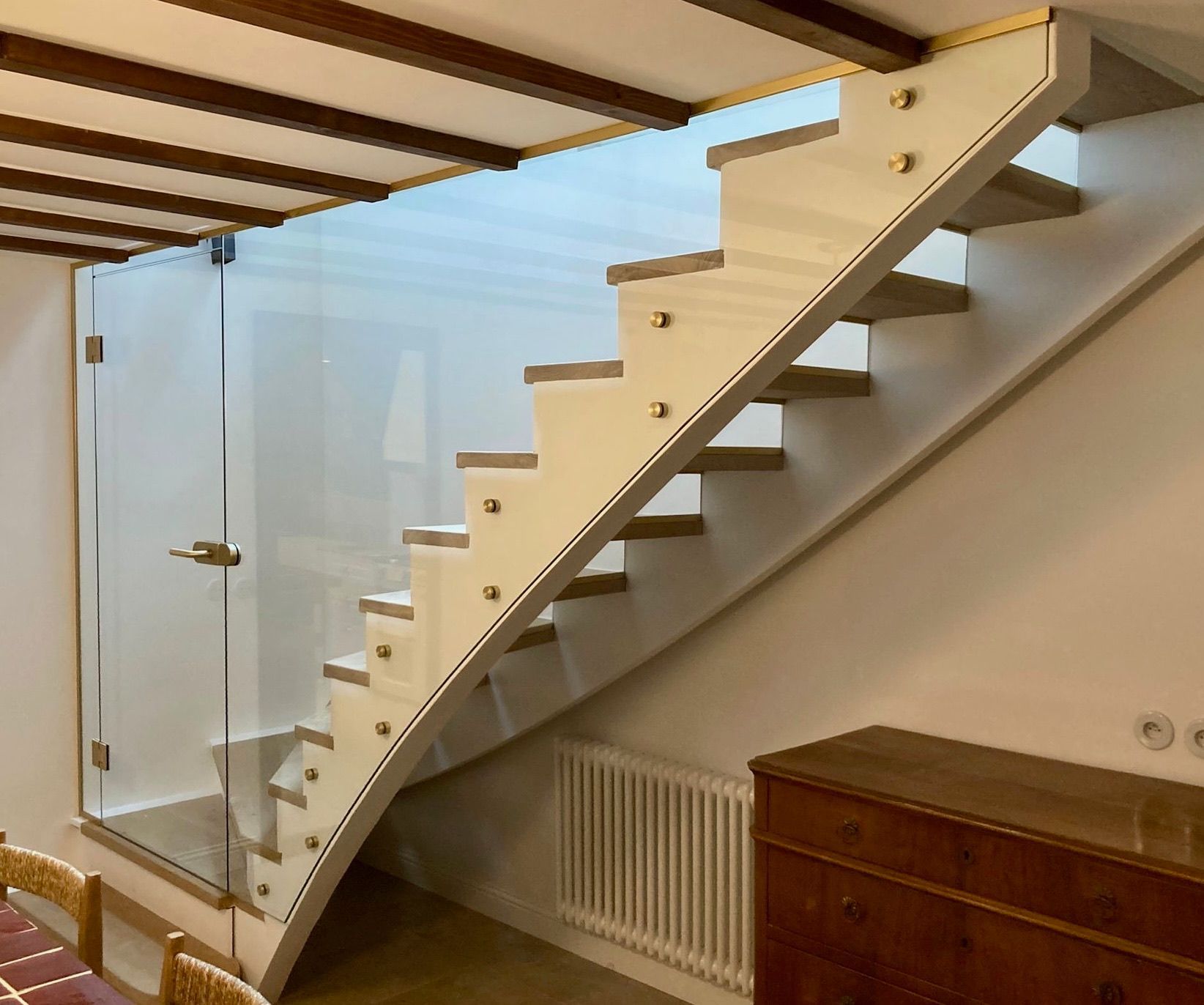 Escalier avec marches en bois et côtés blancs, panneau de verre, accents dorés et plafond en bois.