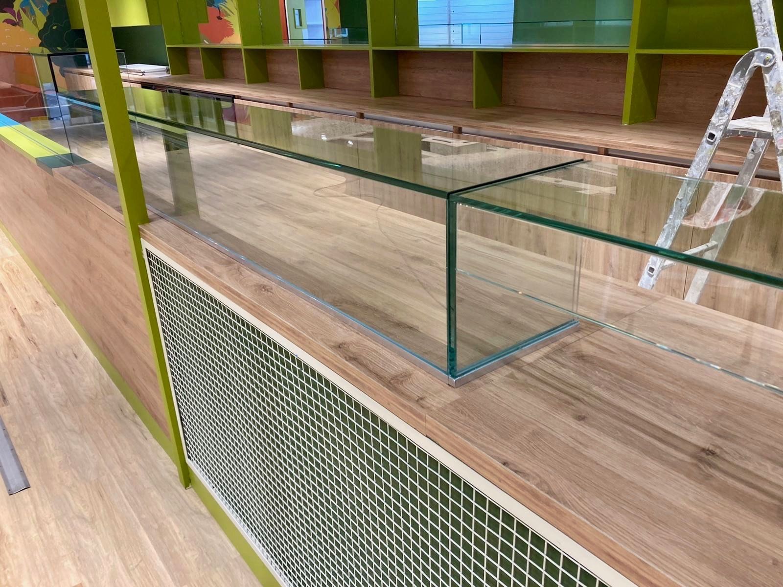 Vitrine en verre sur un comptoir en bois, à côté d'un panneau à motifs verts et blancs, avec des étagères en arrière-plan.