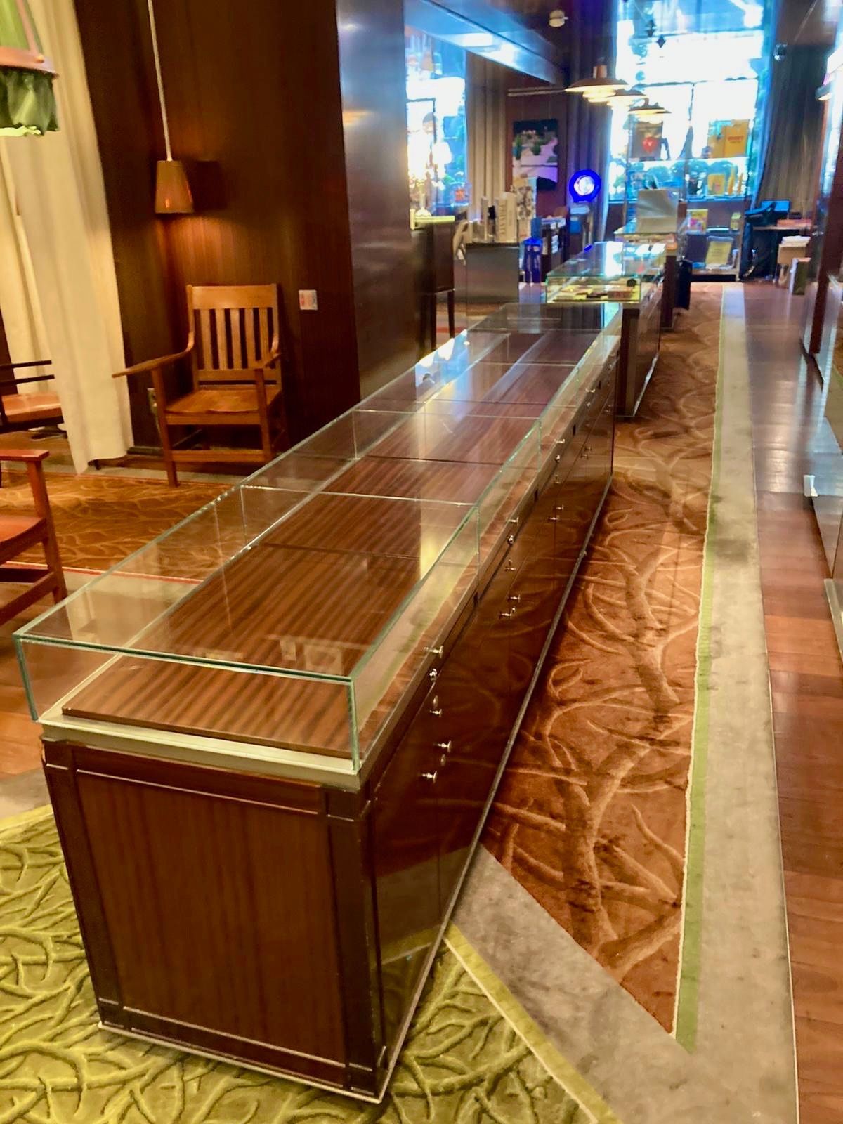 Longue vitrine dans un magasin, en bois brun et en verre, sur une moquette à motifs.