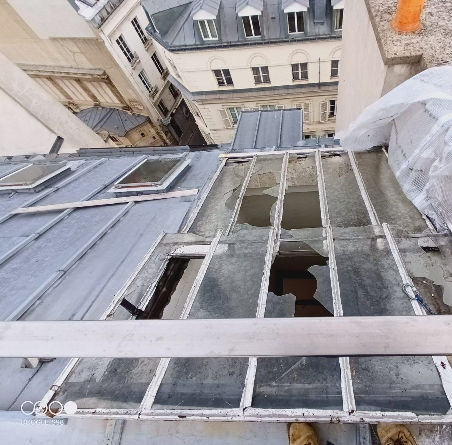 Vue d'un toit à Paris avec des panneaux de verre brisés et les bâtiments environnants.