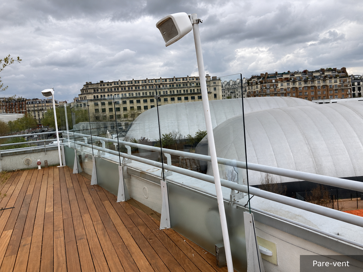Façade d'un bâtiment moderne avec poutres de soutien blanches, panneaux de verre dépoli et trottoir.
