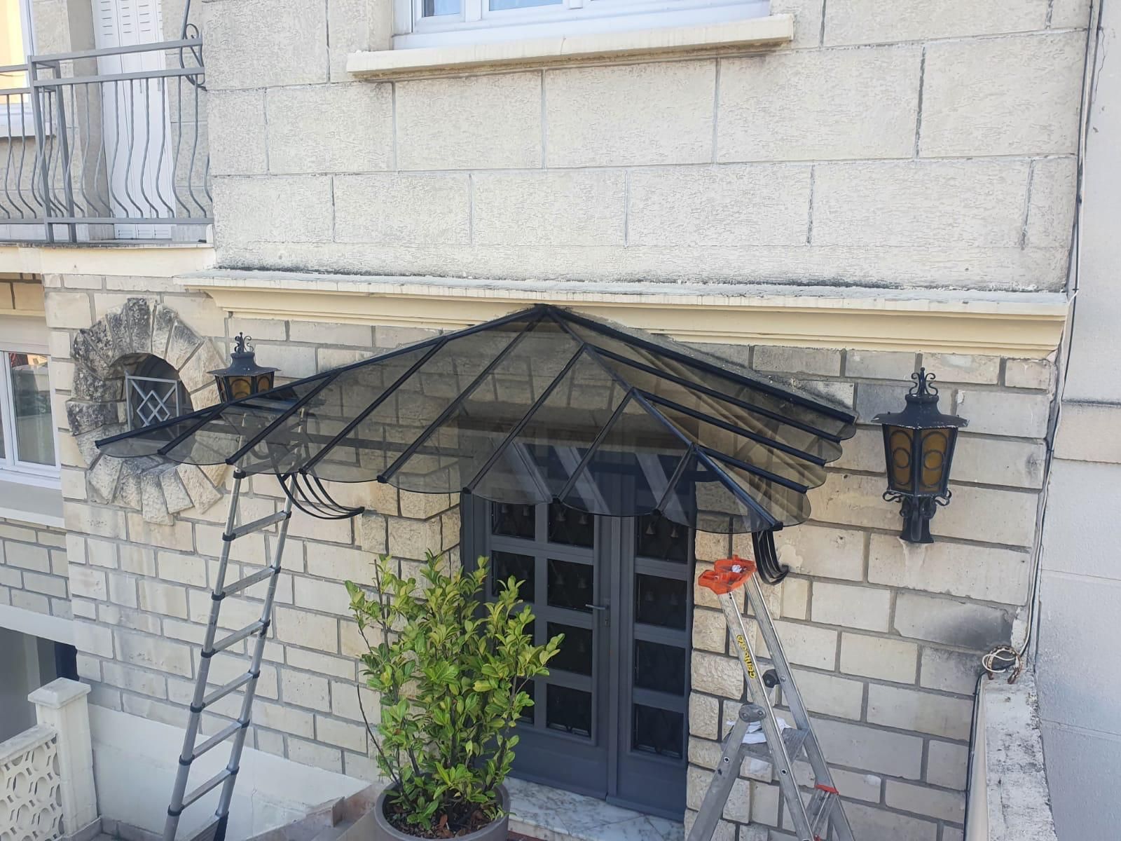 Un auvent gris recouvre une porte grise sur un bâtiment en pierre, deux lanternes de chaque côté.