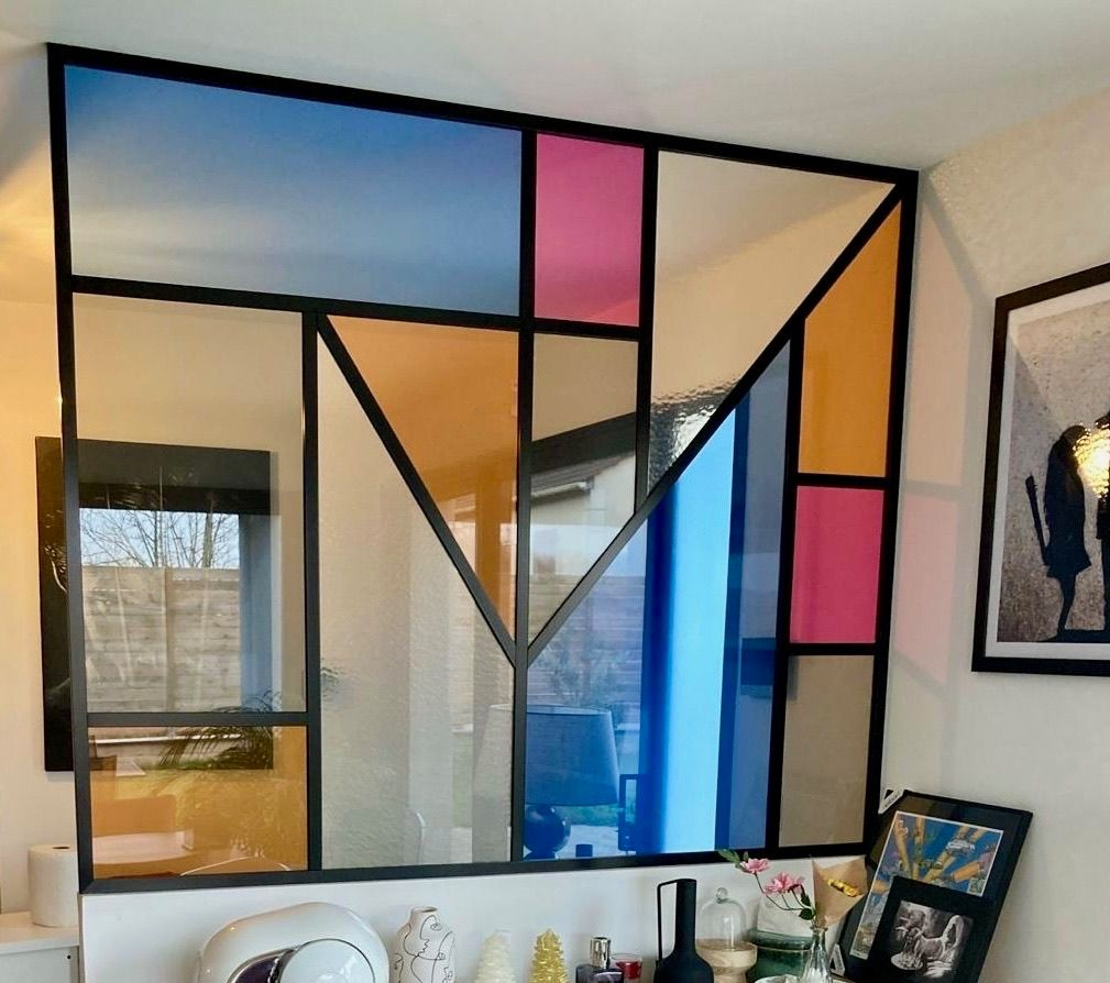 Verrière murale géométrique colorée avec cadre noir et panneaux de verre de couleurs variées.