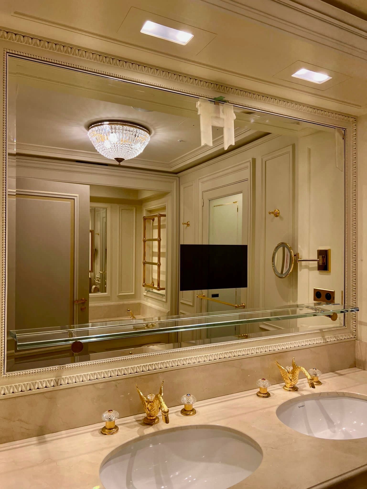 Salle de bains luxueuse avec grand miroir, double vasque, lustre en cristal et touches dorées.