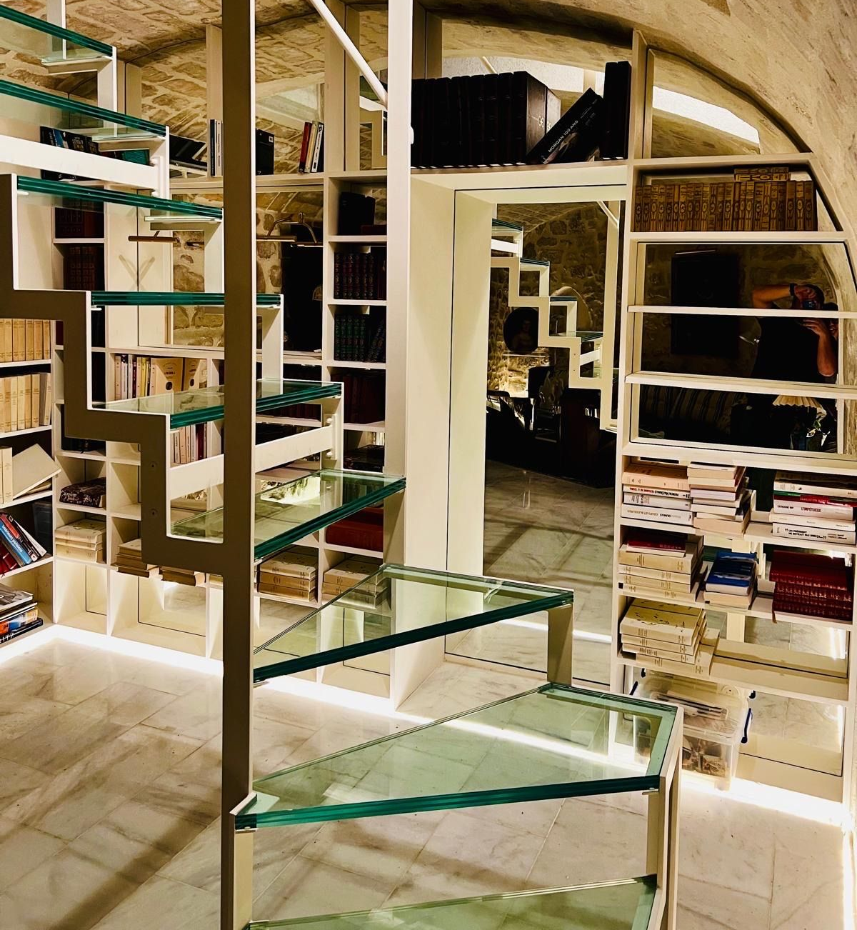 Bibliothèque moderne avec escalier en verre et étagères intégrées.