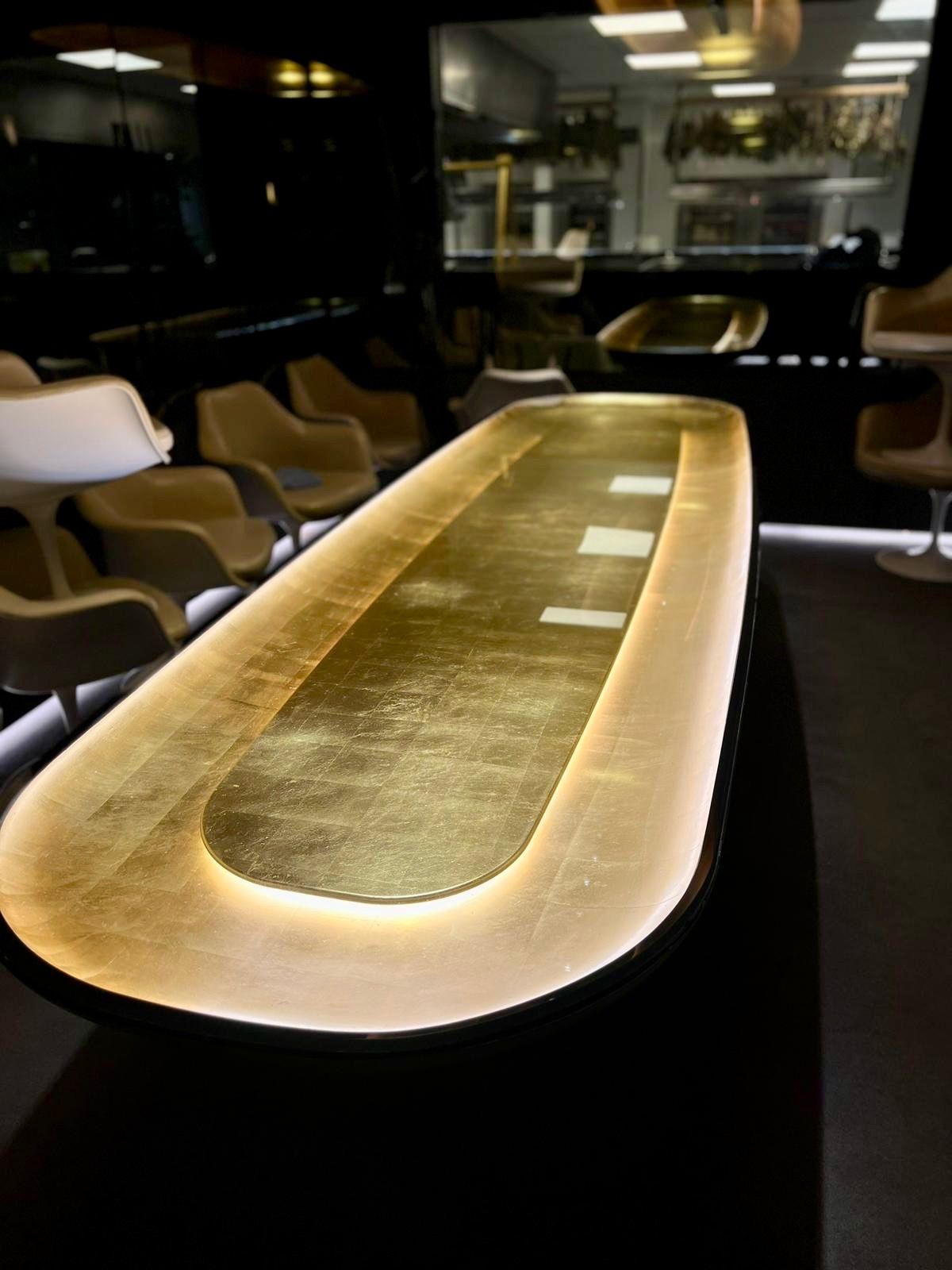 Une longue table au plateau doré avec des lumières intégrées, entourée de chaises.