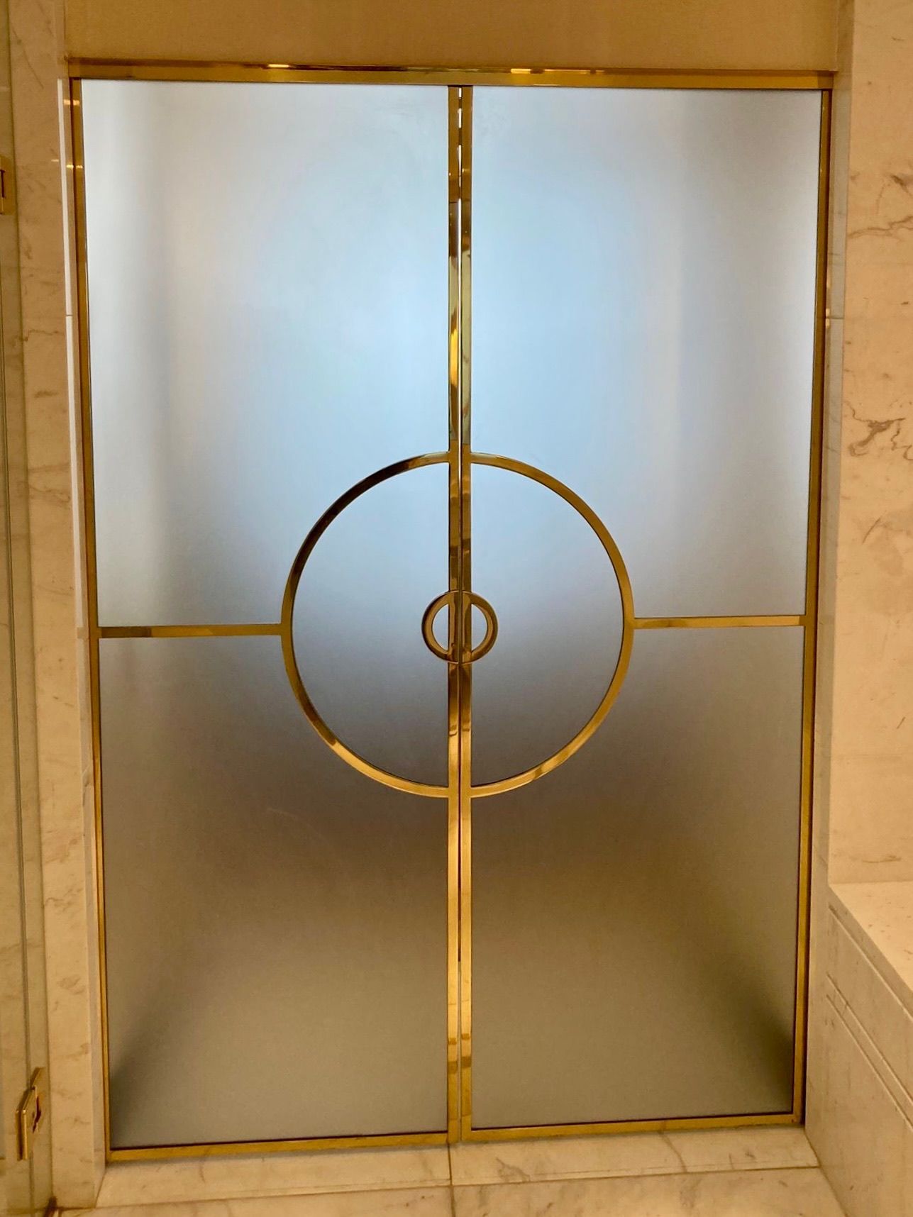 Porte en verre dépoli avec bordure dorée et motif circulaire.