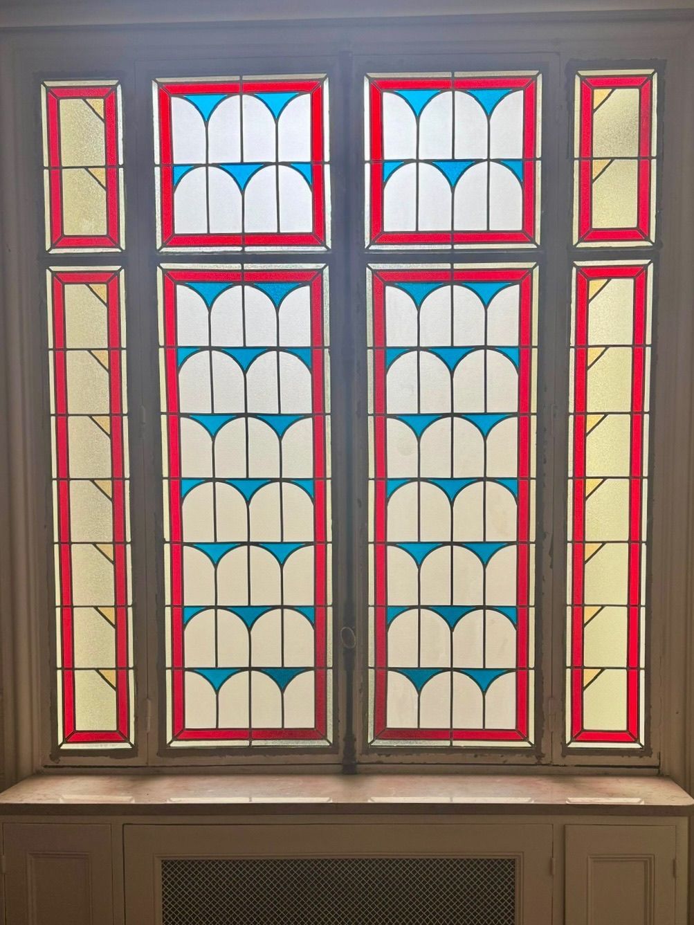 Vitrail à cadres rouges et jaunes, arches bleues et vitres blanches.