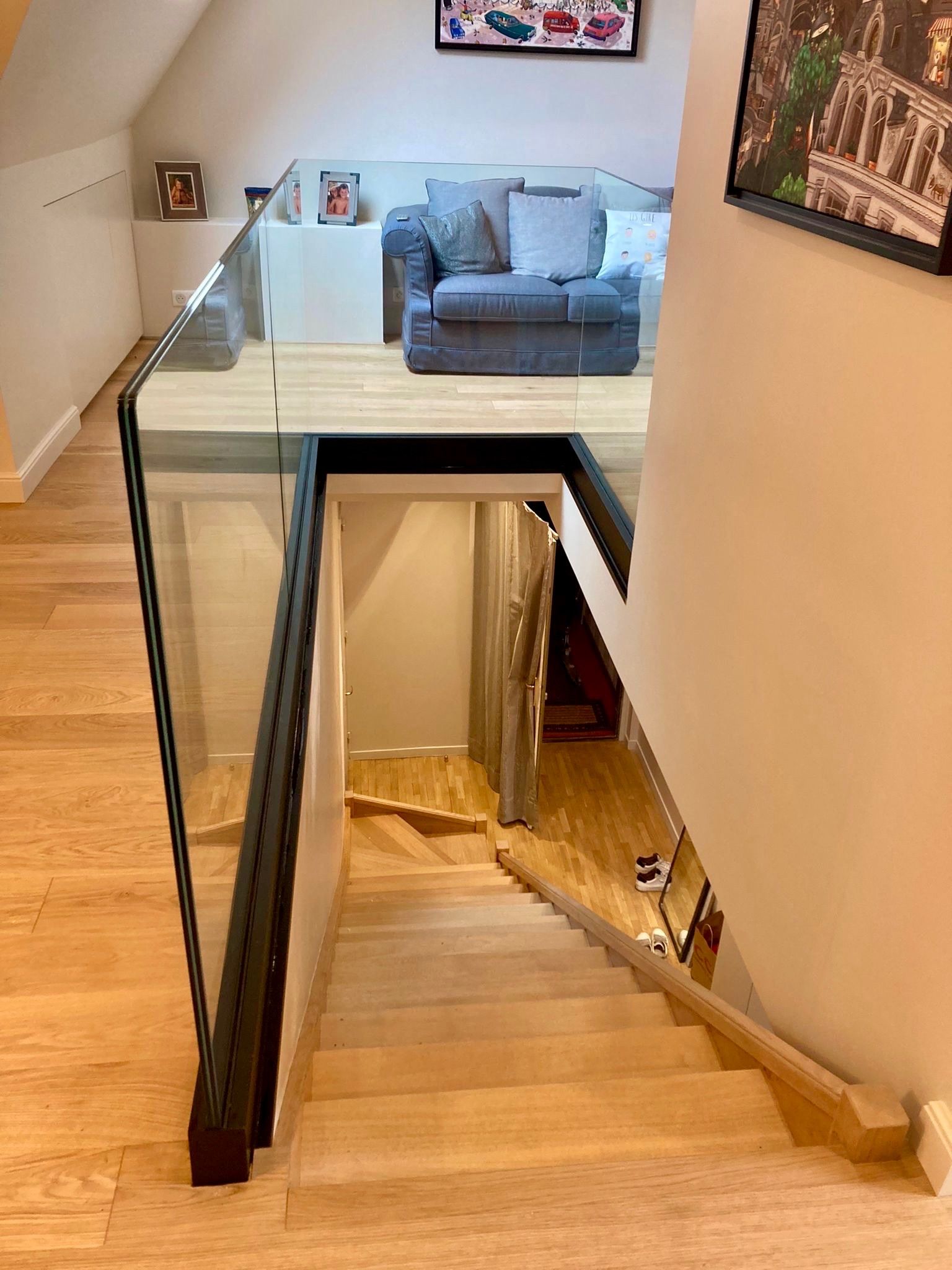 Un escalier en bois mène à une mezzanine avec un garde-corps en verre et un canapé.