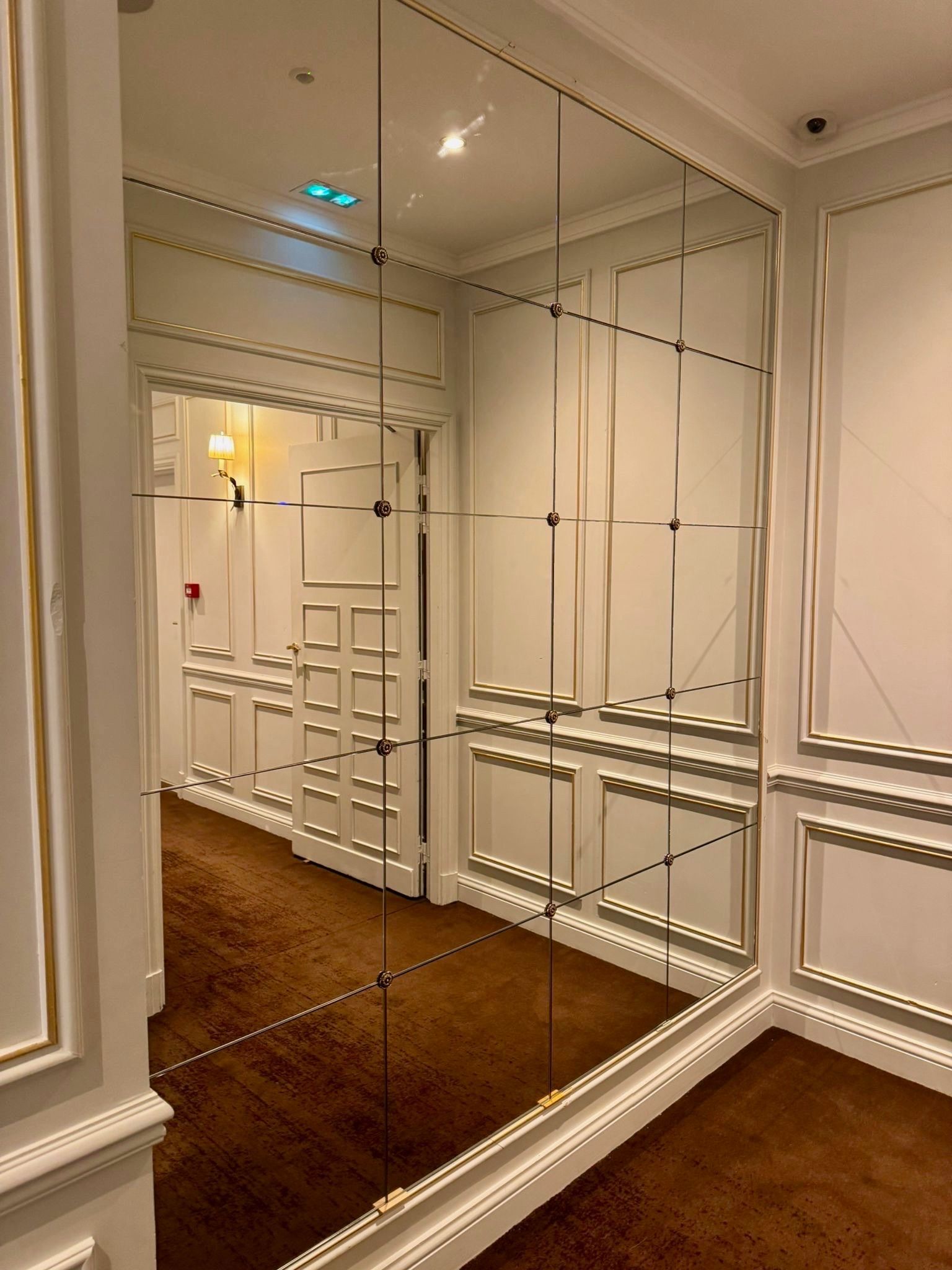 Couloir avec mur en miroir et boiseries blanches ouvragées, moquette marron.