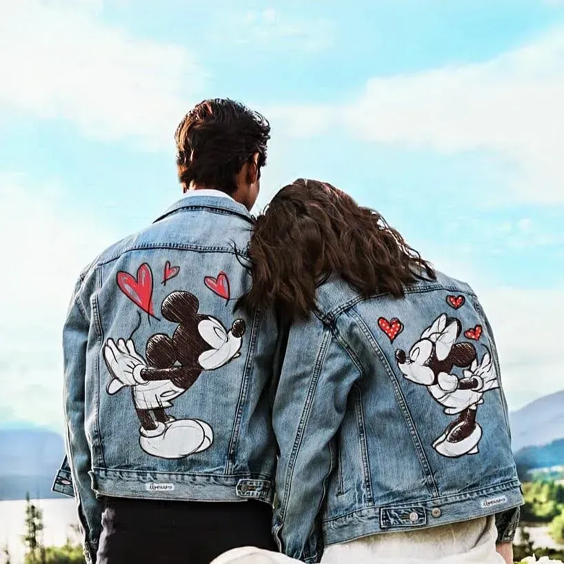 Un hombre y una mujer están parados uno al lado del otro vistiendo chaquetas de mezclilla de Mickey Mouse.