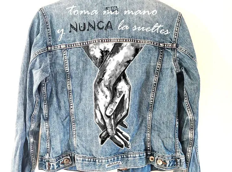 Una chaqueta vaquera con una pintura de dos manos abrazadas en la espalda.