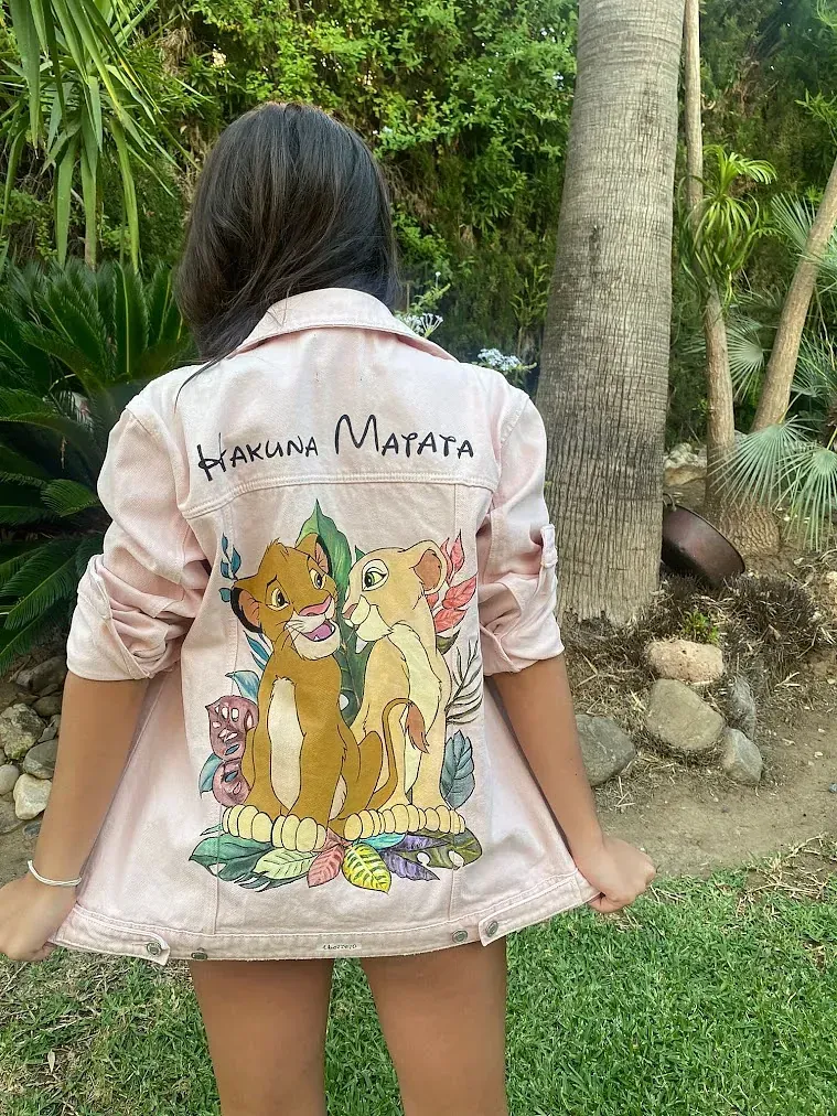 Una niña lleva una chaqueta vaquera rosa con una pintura del rey león en la espalda.