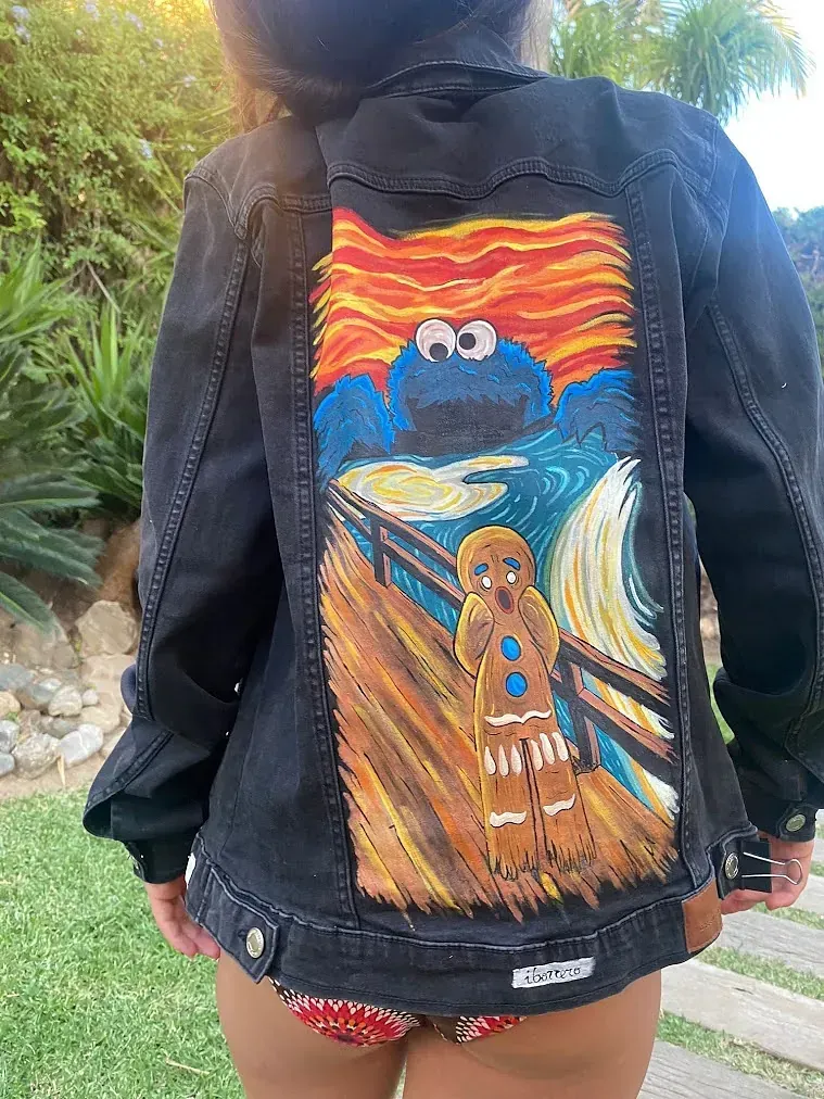 Una mujer lleva una chaqueta vaquera con un dibujo de un monstruo de galletas y un hombre de jengibre en la espalda.