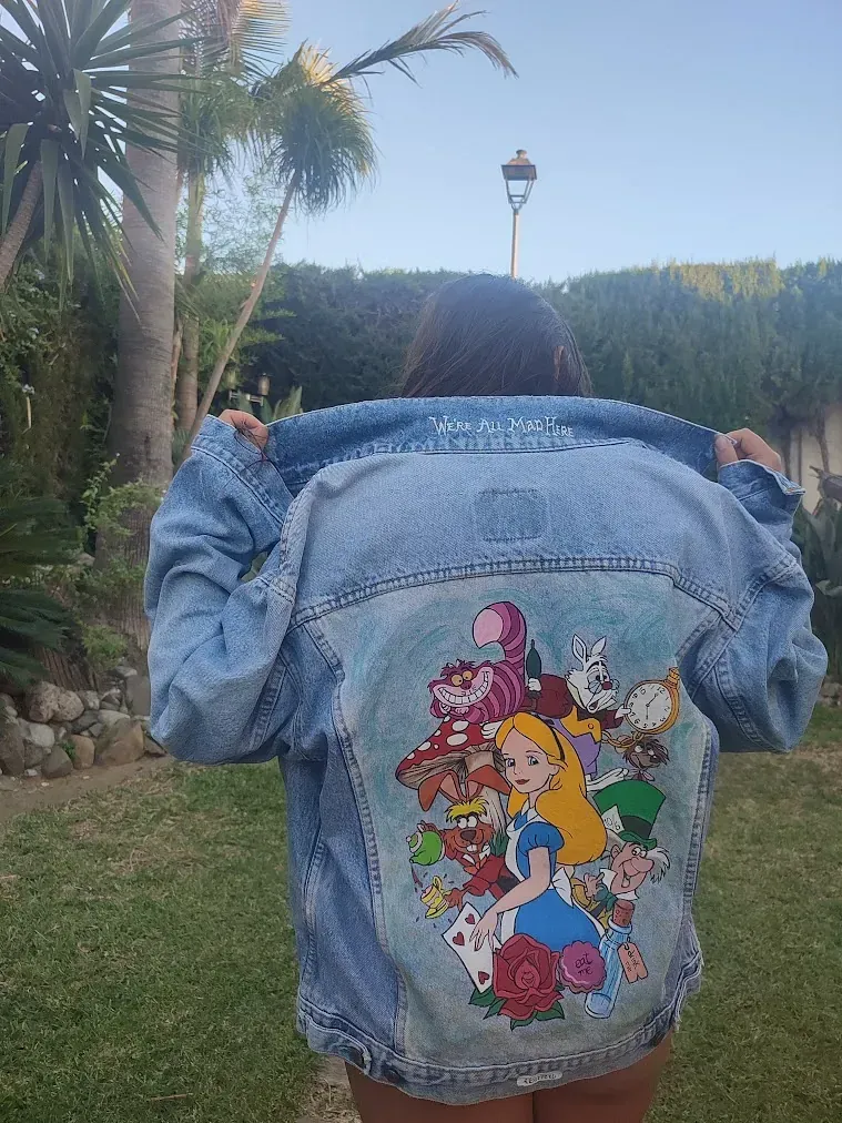 Una mujer lleva una chaqueta vaquera con una pintura de Alicia en el país de las maravillas en la espalda.