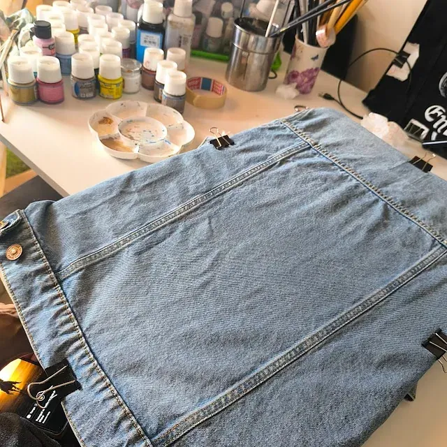 Una chaqueta vaquera está sobre una mesa junto a botellas de pintura.